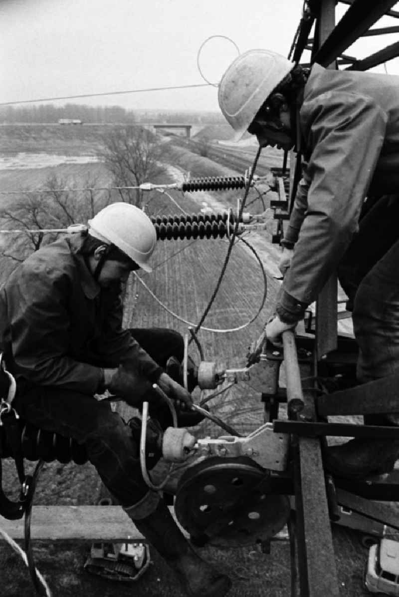 Arbeiter bei der Montage einer Hochspannungsleitung bei Brieselang in luftiger Höhe in Aktion. Die DDR-Energieversorung basiert zu einem großen Teil auf der Verstromung von Braunkohle aus der Lausitz und Sachsen, was unter anderem lange Leitungswege nötig macht.