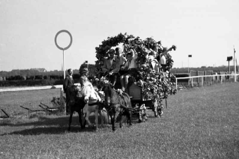 Harvest wagon parade of horticultural and agricultural enterprises on the grounds of the Dresden-Seidnitz racecourse in Dresden in the state Saxony on the territory of the former GDR, German Democratic Republic. Pioneers wear pioneer scarfs on the horse-drawn carriage and wave