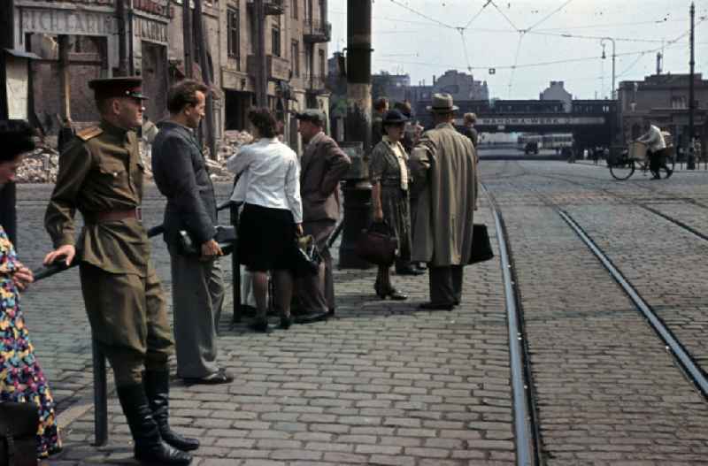 Passengers and a Soviet soldier waiting at the tram-stop Riebeckplatz. Debris in the background in Halle (Saale) in the state Saxony-Anhalt on the territory of the former GDR, German Democratic Republic