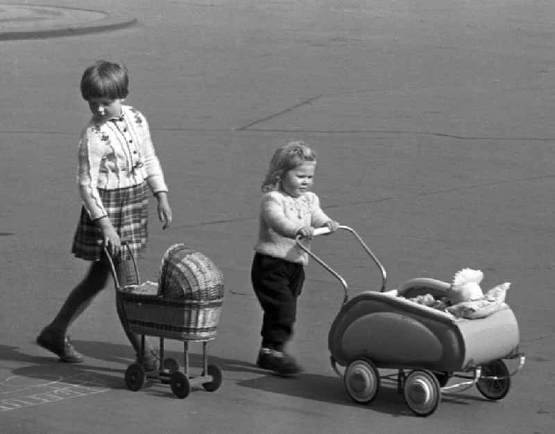 Stolz schiebt das kleine Mädchen den Puppenwagen der großen Schwester vor sich her, die ihren Wagen für kurze Zeit getauscht hat.