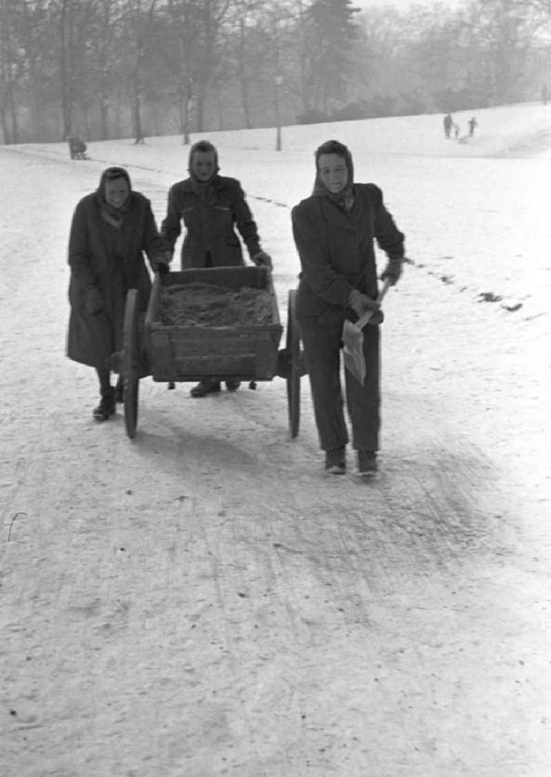 Frauen streuen im Winter mit Karren und Schippe Sand auf die vereisten Fußwege im Clara-Zetkin-Park in Leipzig.