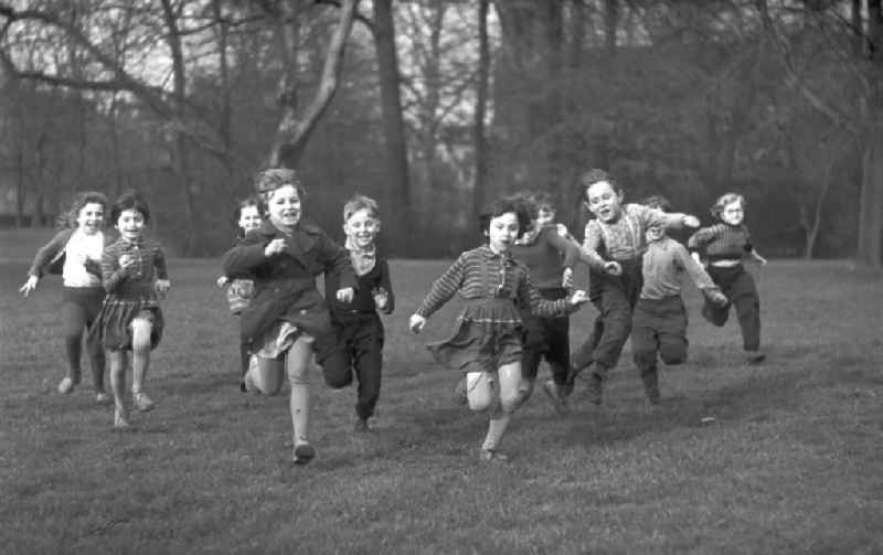 Eine Gruppe Vorschulkinder rennt lachend über eine Wiese im Clara-Zetkin-Park in Leipzig.