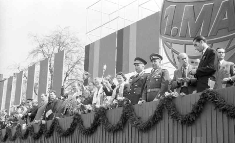 Auf einer Ehrentribüne stehen Vertreter von Politik und Militär bei einem Umzug zum 1. Mai / Maifeiertag. Im Hintergrund ein Aufsteller mit der Aufschrift '1. Mai' in Form eines Globus. Bestmögliche Qualität nach Vorlage!