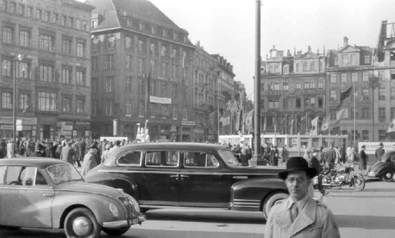 Der Markt während der Frühjahrsmesse. Es herrscht reges Treiben auf dem Platz, viele Passanten sind unterwegs. Im Vordergrund ein PKW / Auto vom Hersteller IFA / Industrieverband Fahrzeugbau und eine Limousine. In der Mitte des Platzes Fahnen mit den Nationen, die an der Messe teilnehmen. Im Frühjahr und im Herbst eines jeden Jahres war die Leipziger Messe Treffpunkt der internationalen Handelswelt.