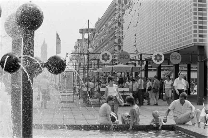 Passers-by at the Kugelbrunnen on Karl-Marx-Strasse ( today Breiter Weg ) in front of the solemnly decorated children's department stores' on the occasion of the 21st Workers' Festival in Magdeburg in the federal state of Saxony-Anhalt in the territory of the former GDR, German Democratic Republic