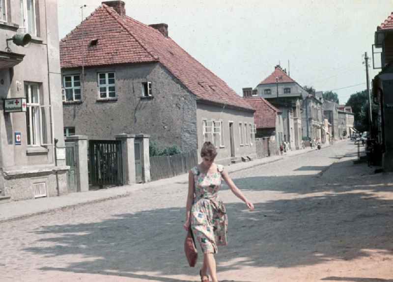 A young woman crosses Schlossstrasse with the Landambulatorium in Neustrelitz in the federal state Mecklenburg-West Pomerania in the area of the former GDR, German democratic republic