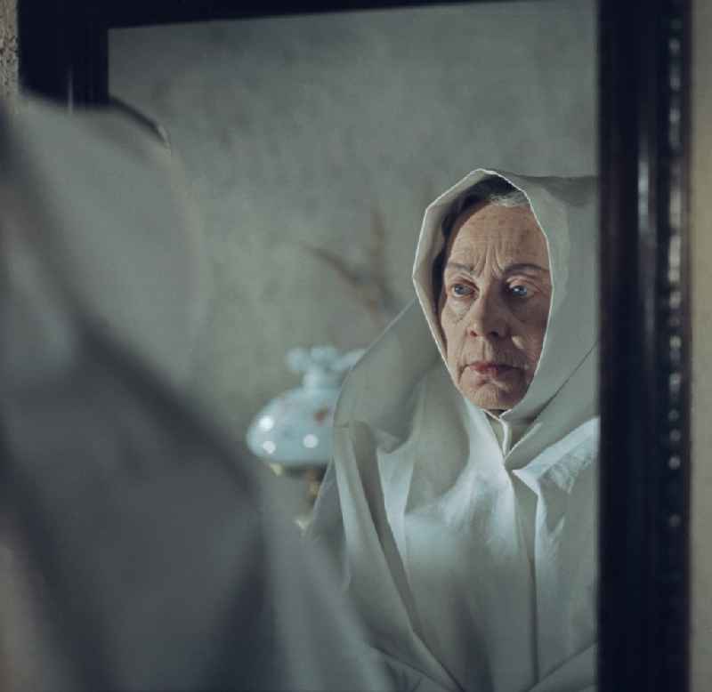 Scene from the film and television production 'Film: Rublak - The Legend of the Surveyed Land' in the town of Heide, Saxony in the area of the former GDR, German Democratic Republic. An old farmer's wife in mourning looks into a mirror. The actress Doris Thalmer as a Sorbian farmer's wife in white costume