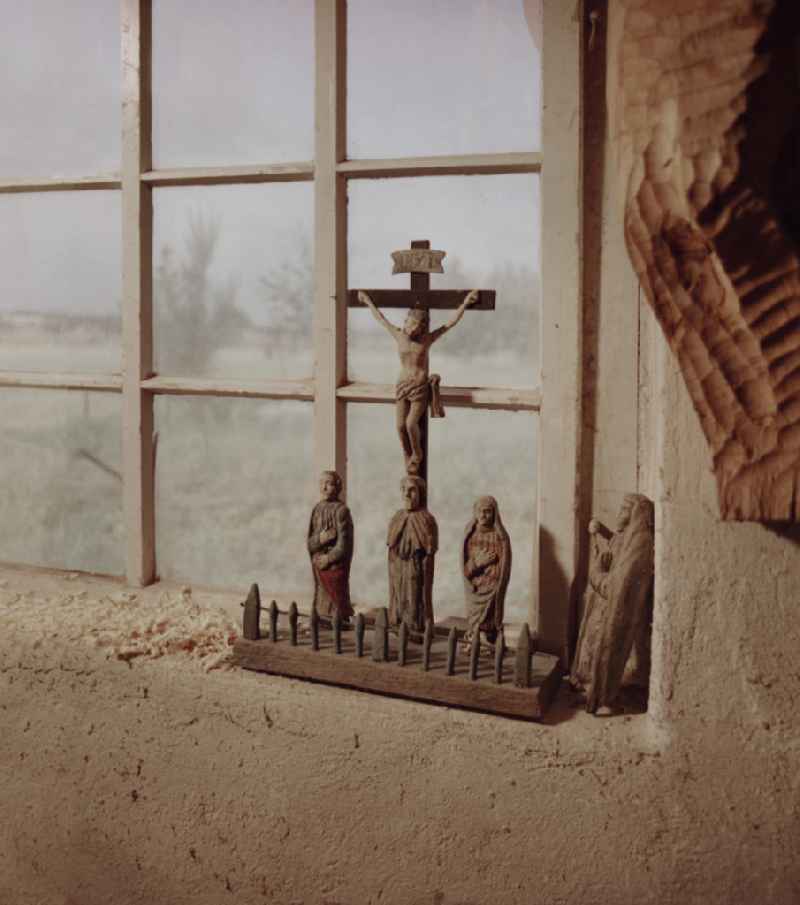 Scene from the film and television production 'Portrait of a Center' Wooden crucifixes in the workshop of the wood restorer Benedikt Dirlich on the main street in Raeckelwitz, Saxony in the area of the former GDR, German Democratic Republic. In front of a window stands a group of wooden figures and a cross with Corpus Christie