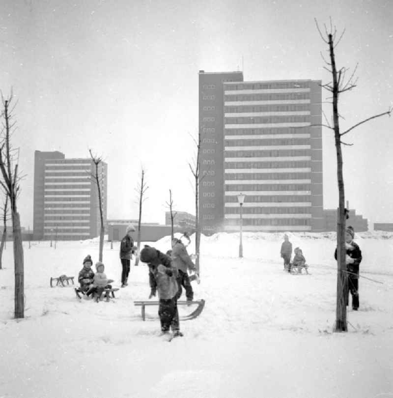 Kinder spielen im Schnee mit Schlitten / Rodelspass, im Hintergrund Plattenbauten von Südstadt.