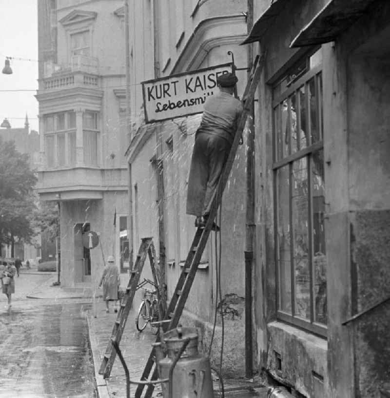 Ein Mann montiert das Schild des Lebensmittelladens 'Kurt Kaiser' in Rostock ab. Das Geschäft mußte einem Textilladen weichen.