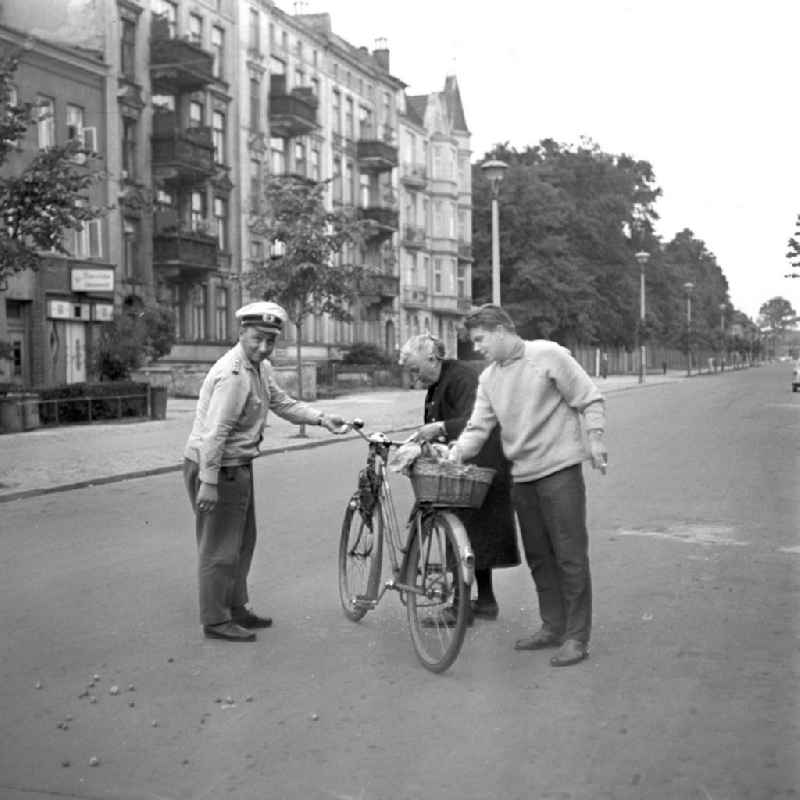Eine alte Frau ist mit ihrem Fahrrad auf einer Straße in Rostock gestürz, ein Passant und ein Verkehrspolizist helfen ihr wieder auf die Beine. Der Einkaufsbeutel am Lenkrad hatte sich in den Speichen verfangen.