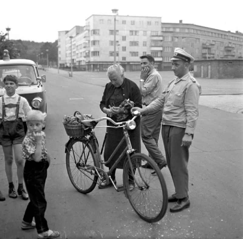 Eine alte Frau ist mit ihrem Fahrrad auf einer Straße in Rostock gestürz, ein Passant und ein Verkehrspolizist helfen ihr wieder auf die Beine. Der Einkaufsbeutel am Lenkrad hatte sich in den Speichen verfangen.