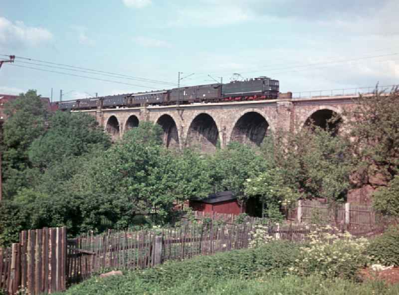 Passenger train powered by an electric locomotive of the Deutsche Reichsbahn drives over a railway bridge on the territory of the former GDR, German Democratic Republic