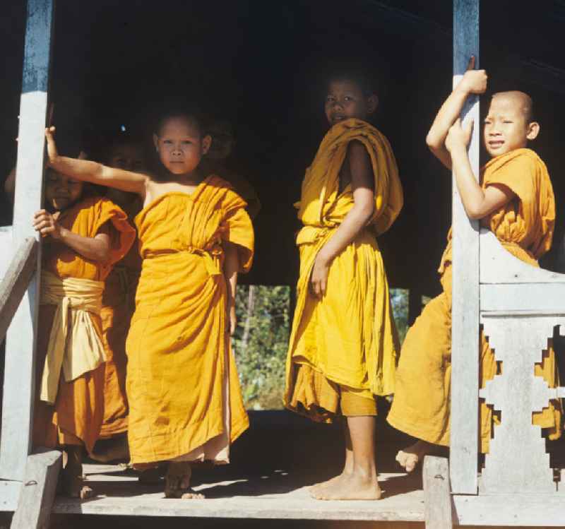 Kindermönche / Mönche in den charakteristischen safrangelben Gewändern in einem buddhistischen Tempel in Vientiane, der Hauptstadt der Demokratischen Volksrepublik Laos. Bis zur Ausrufung der Volksrepublik Laos am 2. Dezember 1975 bestimmte der Theravada-Buddhismus die kulturelle Entwicklung im Land. Nachdem die anfängliche Unterdrückung der traditionellen buddhistischen Bräuche durch die neuen kommunistischen Machthaber mißlang, fand Laos in den folgenden Jahrzehnten einen eigenen Weg der Koexistenz von Buddhismus und Sozialismus.