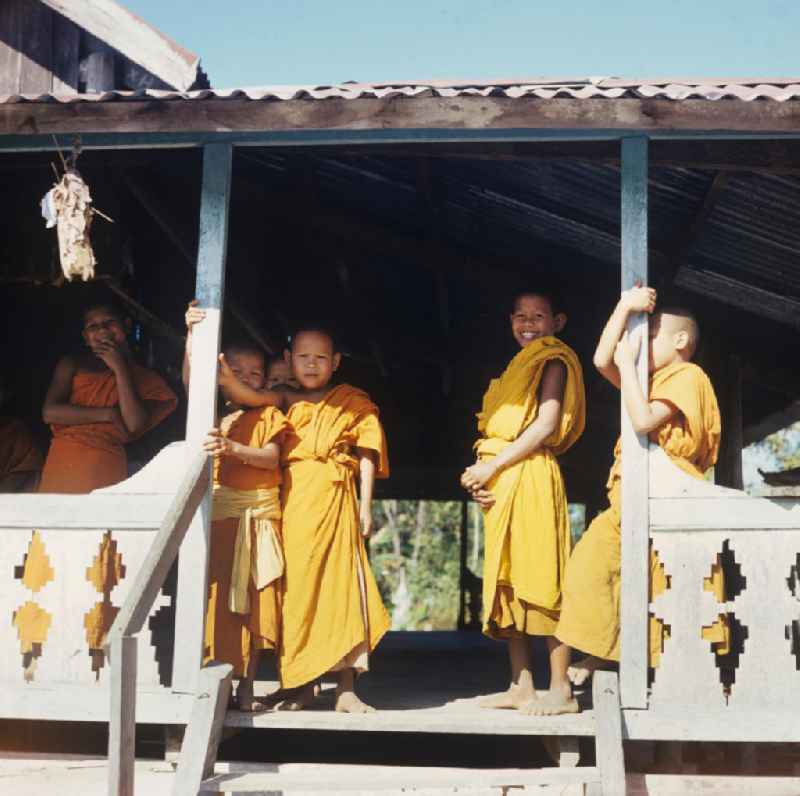 Kindermönche / Mönche in den charakteristischen safrangelben Gewändern in einem buddhistischen Tempel in Vientiane, der Hauptstadt der Demokratischen Volksrepublik Laos. Bis zur Ausrufung der Volksrepublik Laos am 2. Dezember 1975 bestimmte der Theravada-Buddhismus die kulturelle Entwicklung im Land. Nachdem die anfängliche Unterdrückung der traditionellen buddhistischen Bräuche durch die neuen kommunistischen Machthaber mißlang, fand Laos in den folgenden Jahrzehnten einen eigenen Weg der Koexistenz von Buddhismus und Sozialismus.