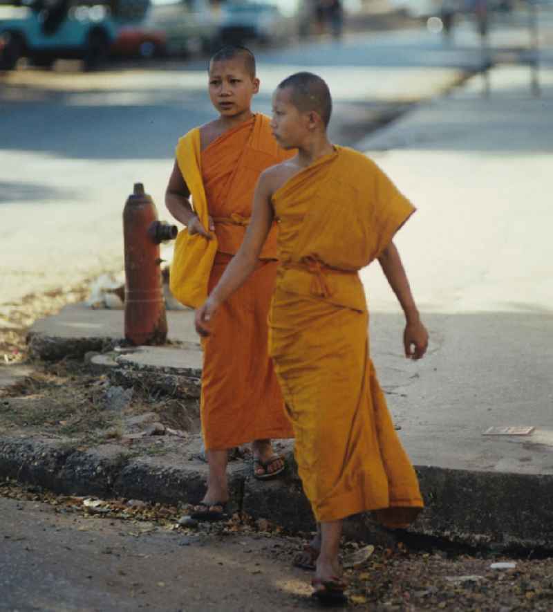 Mönche in den charakteristischen safrangelben Gewändern überqueren eine Straße in Vientiane, der Hauptstadt der Demokratischen Volksrepublik Laos. Bis zur Ausrufung der Volksrepublik Laos am 2. Dezember 1975 bestimmte der Theravada-Buddhismus die kulturelle Entwicklung im Land. Nachdem die anfängliche Unterdrückung der traditionellen buddhistischen Bräuche durch die neuen kommunistischen Machthaber mißlang, fand Laos in den folgenden Jahrzehnten einen eigenen Weg der Koexistenz von Buddhismus und Sozialismus.