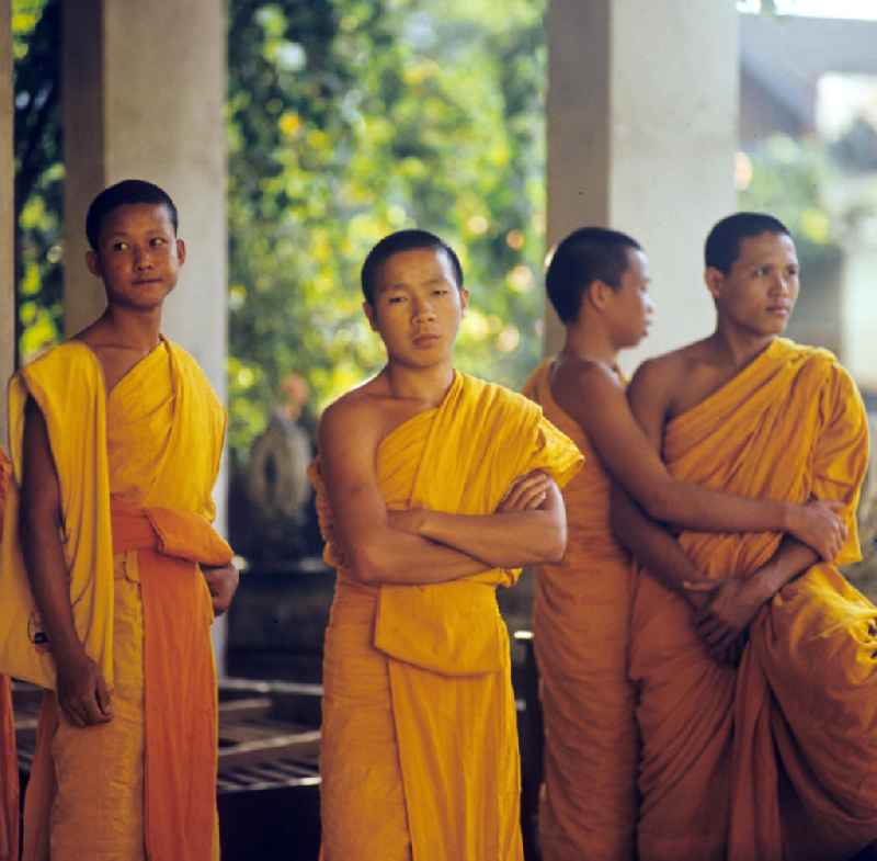 Mönche in den charakteristischen safrangelben Gewändern in einem buddhistischen Tempel in Vientiane, der Hauptstadt der Demokratischen Volksrepublik Laos. Bis zur Ausrufung der Volksrepublik Laos am 2. Dezember 1975 bestimmte der Theravada-Buddhismus die kulturelle Entwicklung im Land. Nachdem die anfängliche Unterdrückung der traditionellen buddhistischen Bräuche durch die neuen kommunistischen Machthaber mißlang, fand Laos in den folgenden Jahrzehnten einen eigenen Weg der Koexistenz von Buddhismus und Sozialismus.