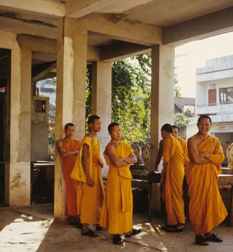 Mönche in den charakteristischen safrangelben Gewändern in einem buddhistischen Tempel in Vientiane, der Hauptstadt der Demokratischen Volksrepublik Laos. Bis zur Ausrufung der Volksrepublik Laos am 2. Dezember 1975 bestimmte der Theravada-Buddhismus die kulturelle Entwicklung im Land. Nachdem die anfängliche Unterdrückung der traditionellen buddhistischen Bräuche durch die neuen kommunistischen Machthaber mißlang, fand Laos in den folgenden Jahrzehnten einen eigenen Weg der Koexistenz von Buddhismus und Sozialismus.