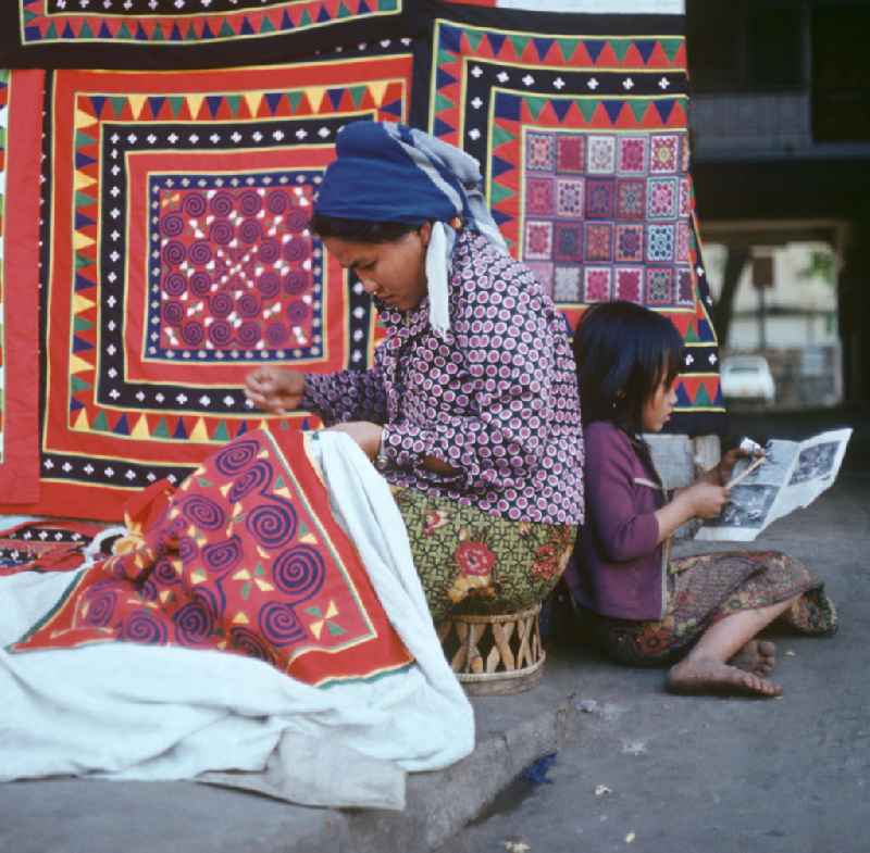 Eine Frau aus dem Volksstamm der Meo, auch Hmong genannt, verkauft selbstgenähte Decken in Vientiane, der Hauptstadt der Demokratischen Volksrepublik Laos. Die Hmong gehörten zu einer infolge des Vietnam-Krieges verfolgten und zurückgezogen lebenden Minderheit in Laos.