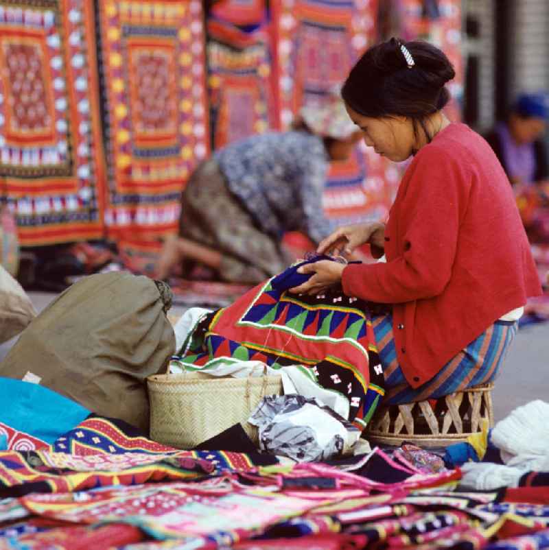 Eine Frau aus dem Volksstamm der Meo, auch Hmong genannt, verkauft selbstgenähte Decken in Vientiane, der Hauptstadt der Demokratischen Volksrepublik Laos. Die Hmong gehörten zu einer infolge des Vietnam-Krieges verfolgten und zurückgezogen lebenden Minderheit in Laos.