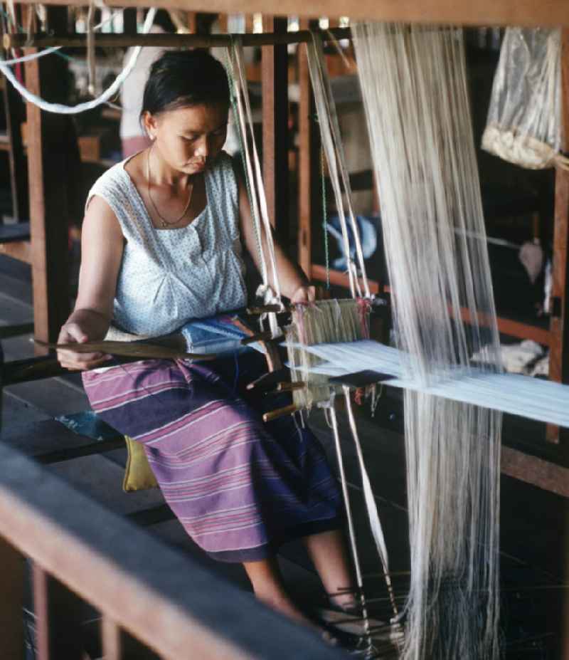 Eine Frau webt an einem Holzwebstuhl in einer Weberei in Vientiane, der Hauptstadt der Demokratischen Volksrepublik Laos.