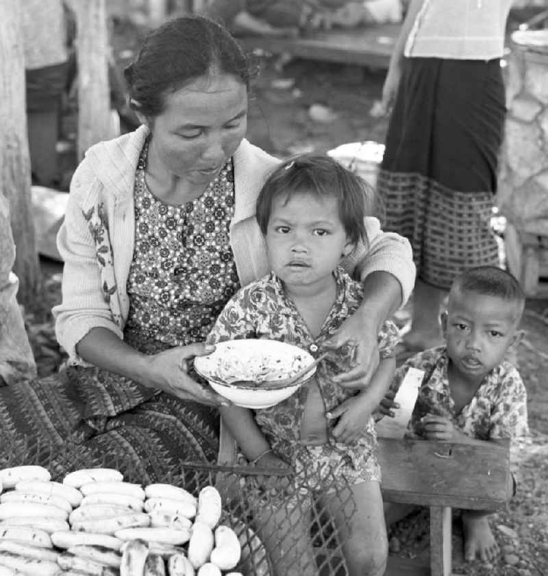 Frau mit Kindern hinter ihrem Marktstand in Vientiane, der Hauptstadt der Demokratischen Volksrepublik Laos.