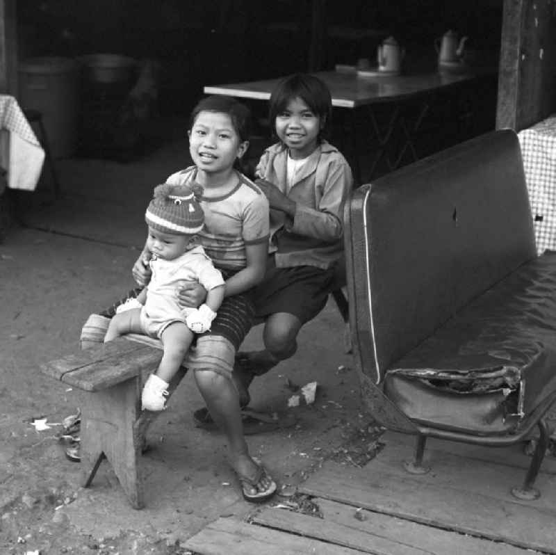 Mädchen sitzen auf einer Bank vor ihrem Haus und flechten sich die Haare in Vientiane in der Demokratischen Volksrepublik Laos.