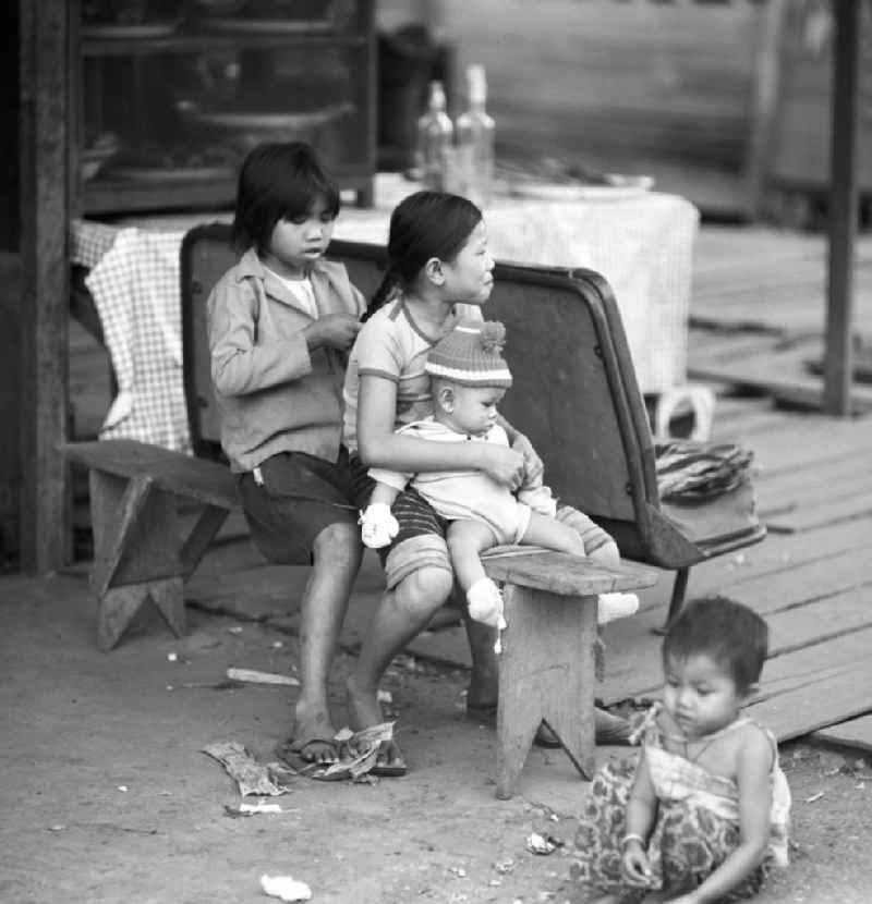 Mädchen sitzen auf einer Bank vor ihrem Haus und flechten sich die Haare in Vientiane in der Demokratischen Volksrepublik Laos.