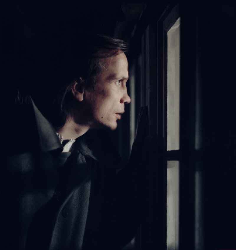 Scene from the film and television production 'Rublak - The Legend of the Surveyed Land' in the Haide district of Weisskeissel, Saxony in the area of the former GDR, German Democratic Republic. The actor Christian Grashof stands at the house at night and looks through the window into the farmhouse parlor