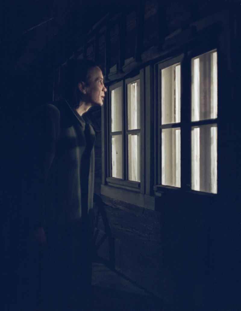 Scene from the film and television production 'Rublak - The Legend of the Surveyed Land' in the Haide district of Weisskeissel, Saxony in the area of the former GDR, German Democratic Republic. The actor Christian Grashof stands at the house at night and looks through the window into the farmhouse parlor