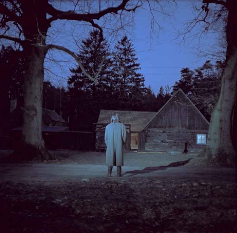 Scene from the film and television production 'Rublak - The Legend of the Surveyed Land' in the Haide district of Weisskeissel, Saxony in the area of the former GDR, German Democratic Republic. The actor Christian Grashof stands in front of it like a shadow and looks towards the entrance of a farmhouse