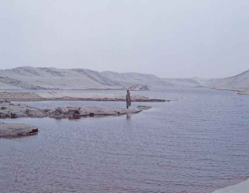 Scene from the film and television production 'Rublak - The Legend of the Surveyed Land' in Weisswasser/Oberlausitz, Saxony in the area of the former GDR, German Democratic Republic. The actor Christian Grashof stands alone on a small sandy peninsula in the middle of a lake in a waste landscape of a brown coal open-cast mine