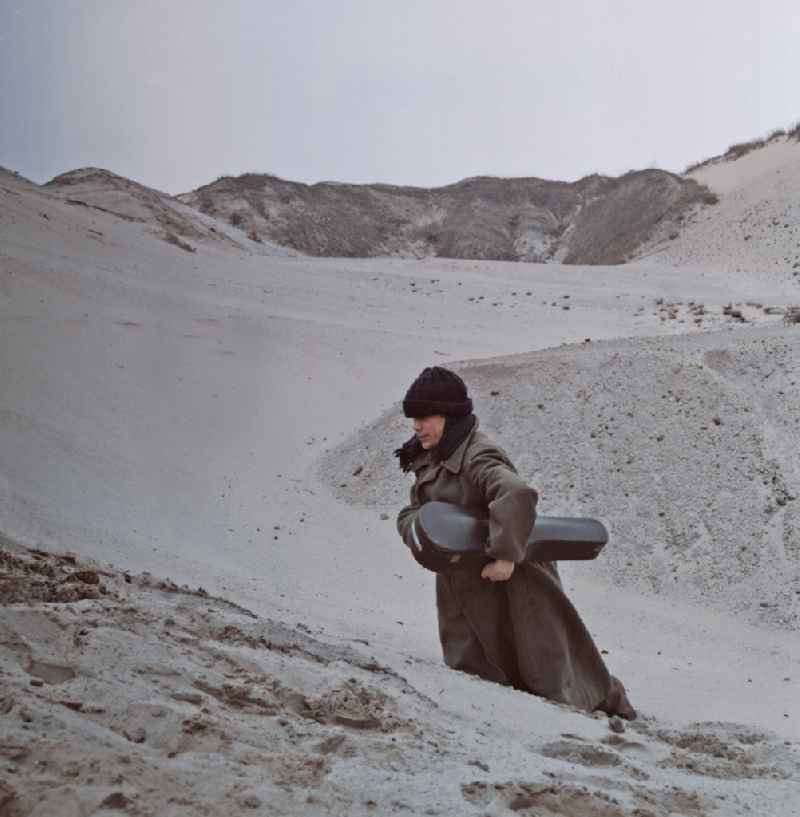 Scene from the film and television production 'Rublak - The Legend of the Surveyed Land' in Weisswasser/Oberlausitz, Saxony in the area of the former GDR, German Democratic Republic. The actor Christian Grashof walks with a violin case under his arm through the sandy plain in the waste landscape of a brown coal open-cast mine